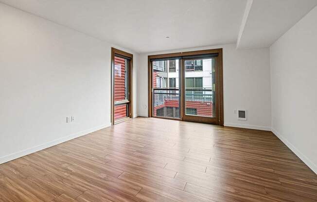 A room with wooden flooring and a large window with a view of a cityscape.