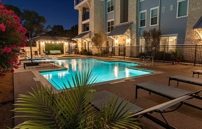 A pool surrounded by lounge chairs and plants at night.