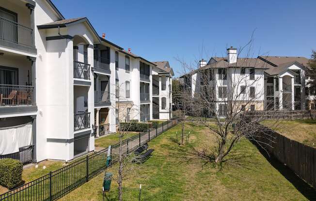 A row of white apartment buildings with black fences and green bushes.