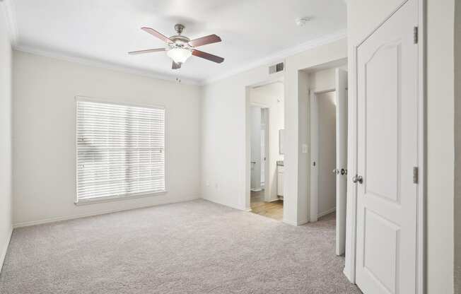 an empty bedroom with a ceiling fan and a door to a bathroom