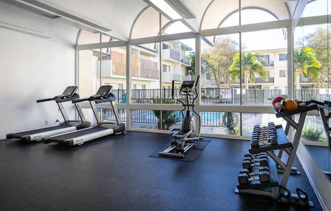 a gym with treadmills and weights in a building with large windows