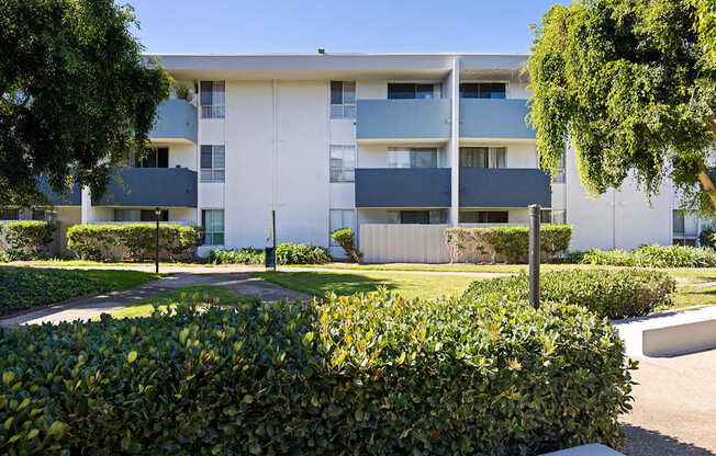 A white and grey building with a green bush in the foreground.