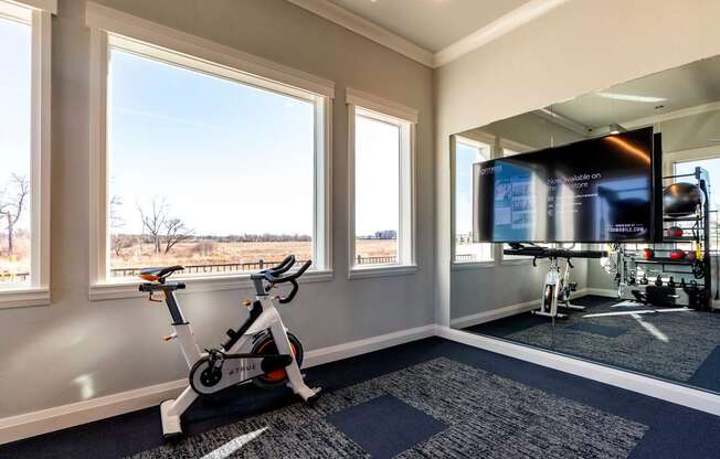 A room with a stationary bike and a TV showing a gym workout.