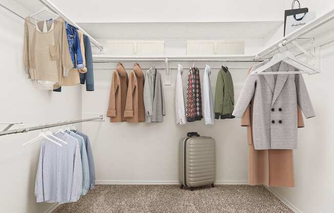 a closet with clothes hanging on a rack and a suitcase