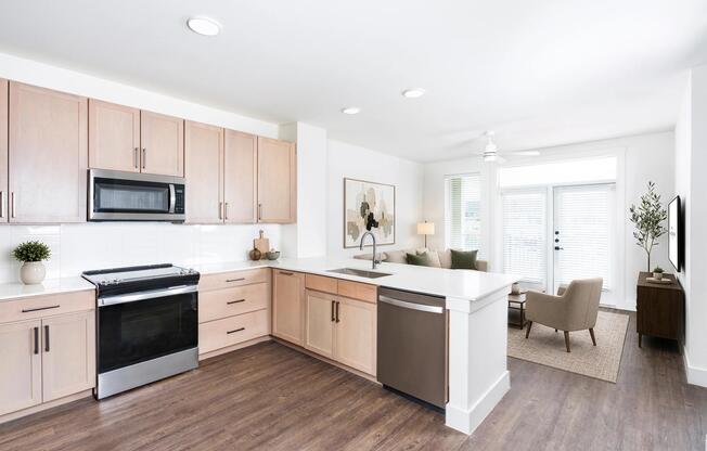 Open kitchen with light wood cabinetry, a spacious island, and seamless flow into the living area filled with natural light and soft finishes.
