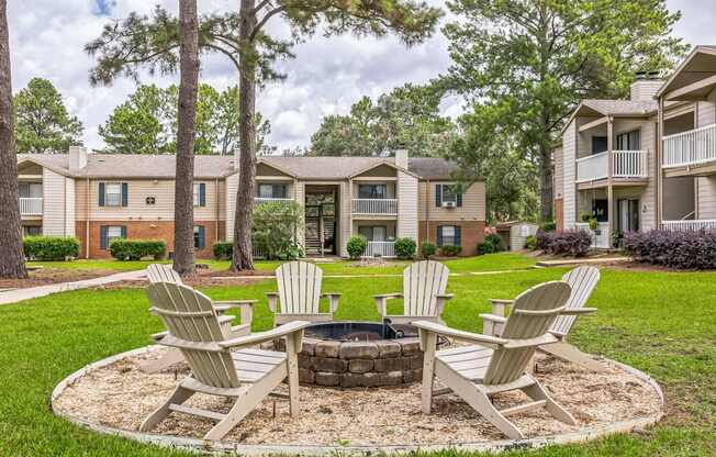 A fire pit surrounded by four chairs in a grassy area with apartment buildings in the background.