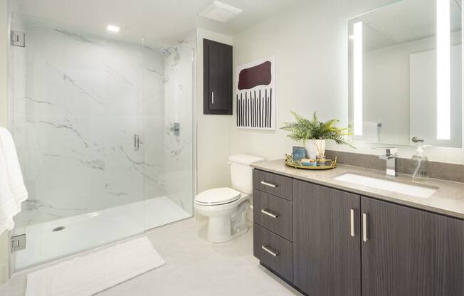 Studios in Woodland Hills, CA - The Q Variel - Bathroom with Quartz Countertops, Wood-Style Cabinets, a Shower with Marble Walls, and Tile Hard-Surface Flooring