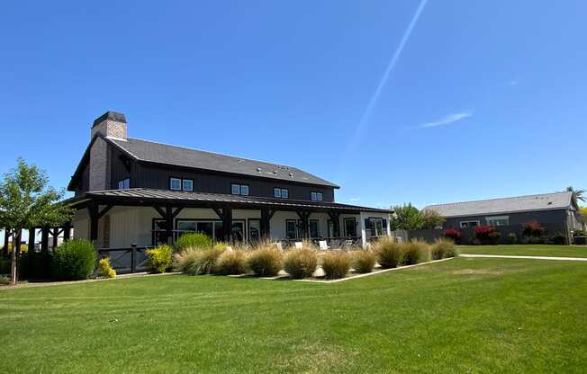 A large building with a black roof and white walls is surrounded by a grassy area and some bushes.
