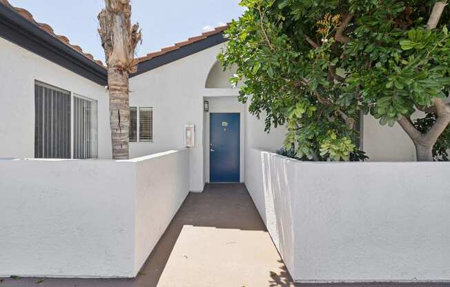 the entrance to a white house with a blue door and trees