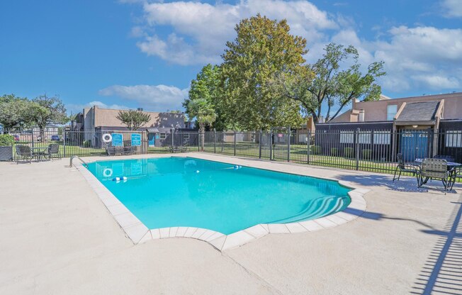 A pool surrounded by a fence and trees at The Drake in Bossier City, LA