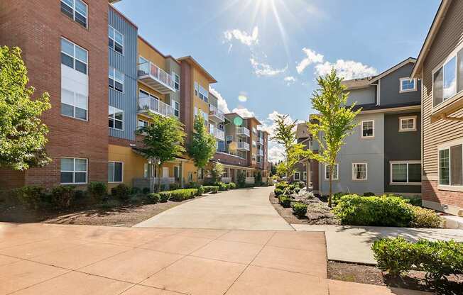 A sunny day in a residential area with apartment buildings on both sides of a tree-lined street.