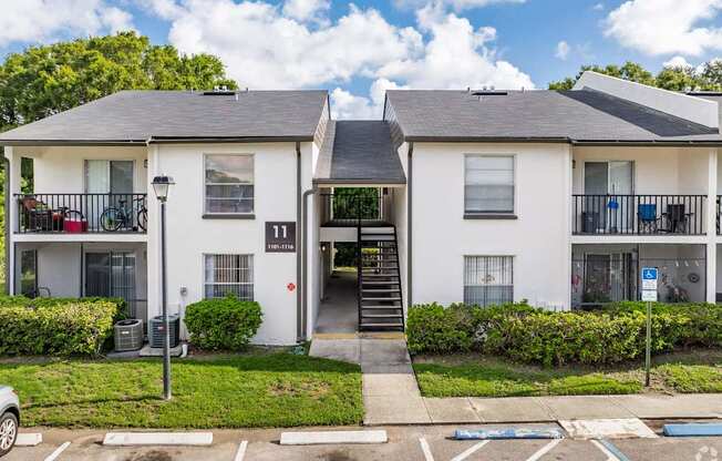 A white two-story apartment building with a black roof and a parking lot in front.