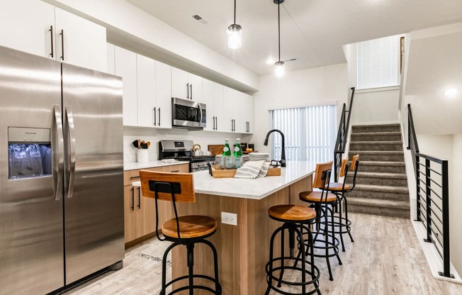 a kitchen with a counter with bar stools and a stainless steel refrigerator