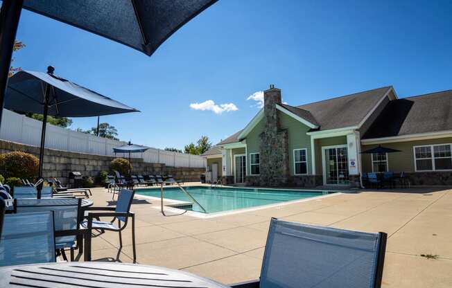 a swimming pool in front of a house with chairs and umbrellas