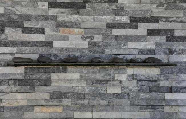 A wall made of grey stone blocks with a black shelf on top.