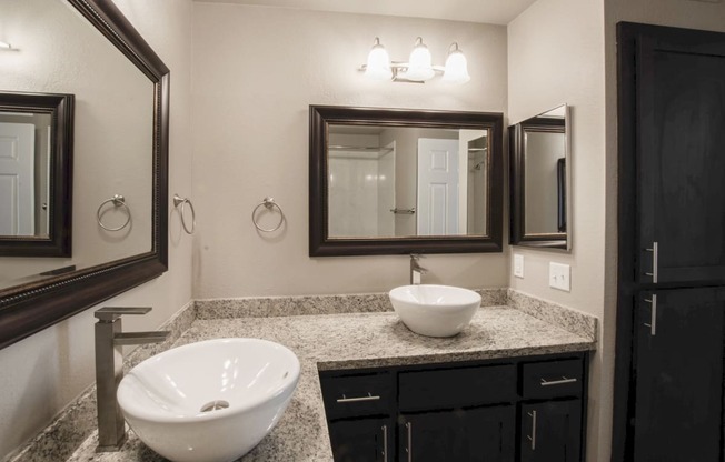 View of bathroom vanity with two vessel sinks and two mirrors with lighting