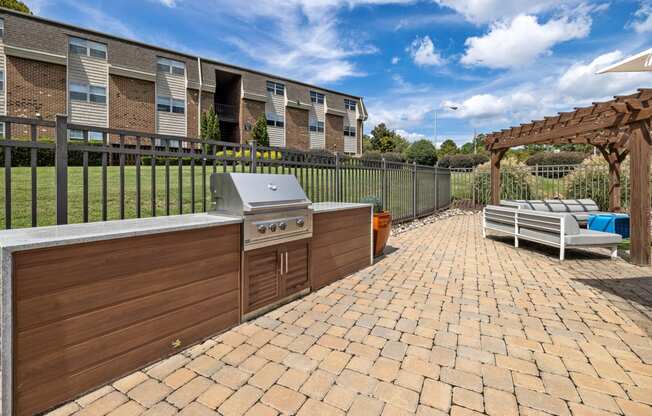 a brick patio with a barbecue and lounge chairs
