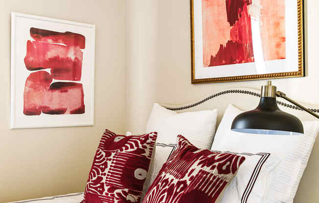 a bedroom with red and white pillows and artwork on the wall