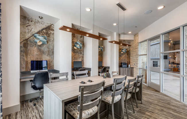 A modern office space with a long table and chairs, a brick wall, and a glass door leading to another room.
