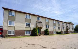 A three-story apartment building with grassy area, and clear blue sky.