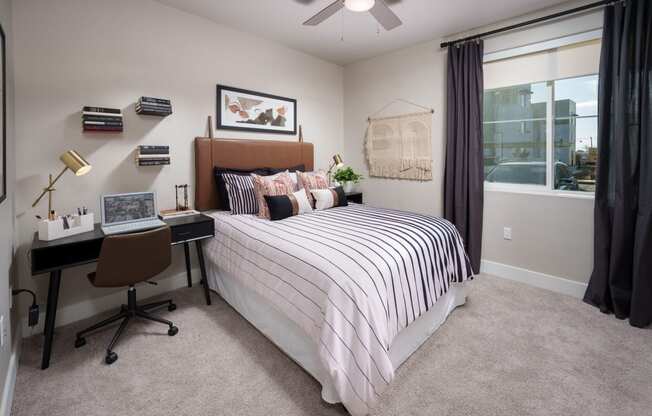 Rancho Cordova, CA Garden-Style Apartments with an In-Unit Washer and Dryer - Aurora - Bedroom with Plush Carpeting, Bed, Desk with Lamp, Chair, Nightstand with Lamp, Ceiling Fan, and Large Window.