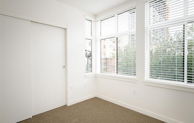 an empty bedroom with three windows and a closet