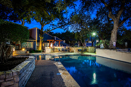 A pool surrounded by a stone wall and trees at night.