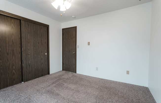 A room with a carpeted floor and two wooden doors. at Bristol Ridge, Urbandale, Iowa