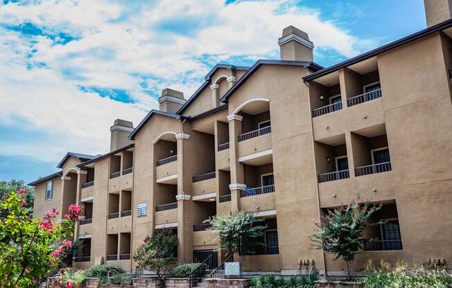 A large apartment complex with balconies and flower bushes in front.