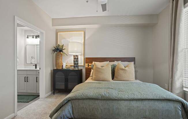 Flatiron West Trade Apartments staged model unit bedroom with gray carpet, attached bathroom with walk-in closet, and a ceiling fan