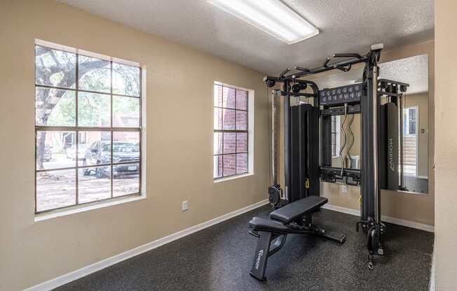 A home gym with a squat rack, bench, and windows.