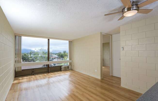 an empty living room with wood floors and a large window at Palms of Kilani Apartments, Wahiawa, HI, 96786