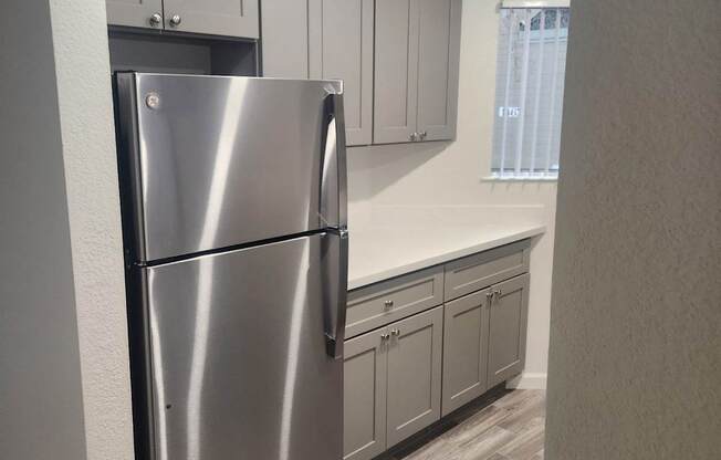 A stainless steel refrigerator in a kitchen with wooden flooring and white walls.