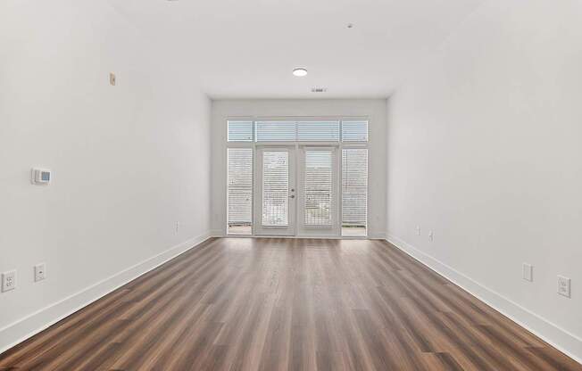 A room with wooden floors and a white wall with a door at the end.