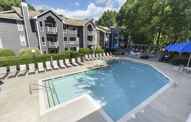 A swimming pool surrounded by lounge chairs and umbrellas in front of apartment buildings.