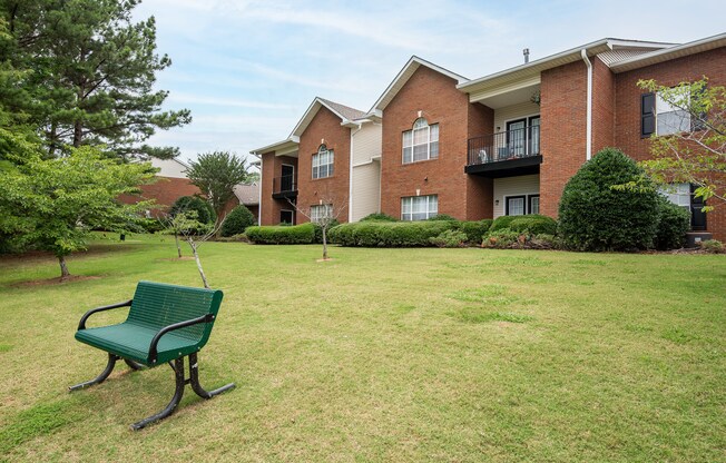 a park bench sits in the grass in front of an apartment building