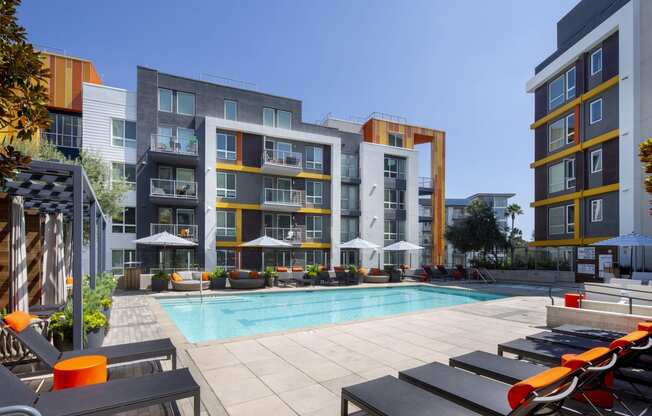 a pool with lounge chairs in front of an apartment building