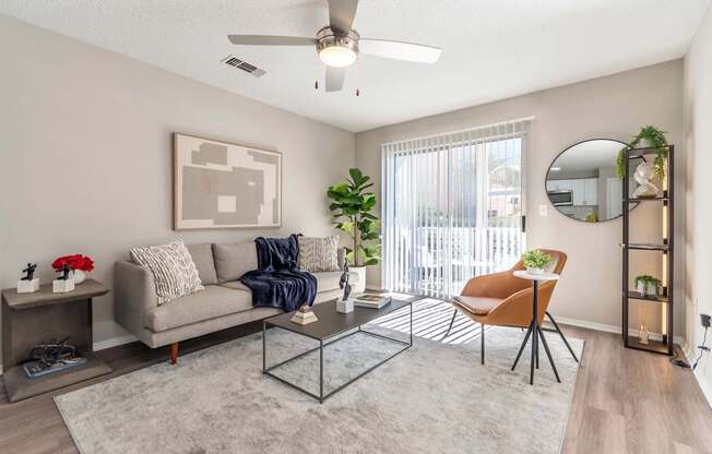 A living room with a grey couch, a glass coffee table, and a ceiling fan.
