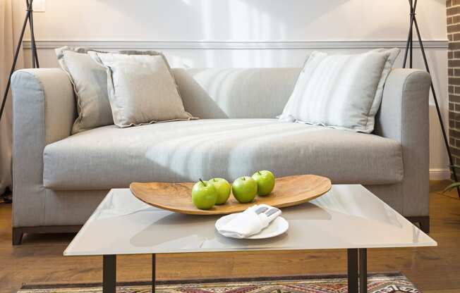 a living room with a gray couch and a coffee table with green apples on it