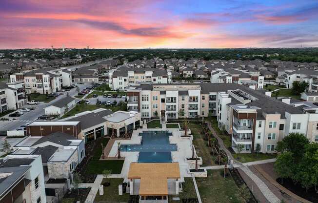 A sunset view of a residential area with apartment buildings and a pool.