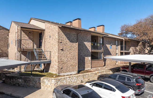 A stone apartment building with a parking lot in front at Preston Oaks Apartments in Dallas, TX.