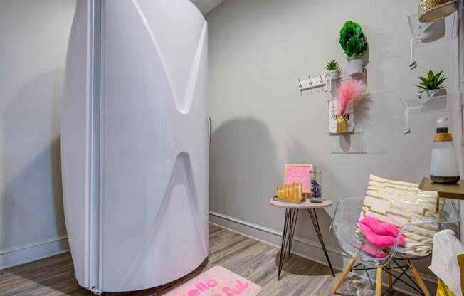 A white refrigerator stands in a room with a pink rug and a chair.