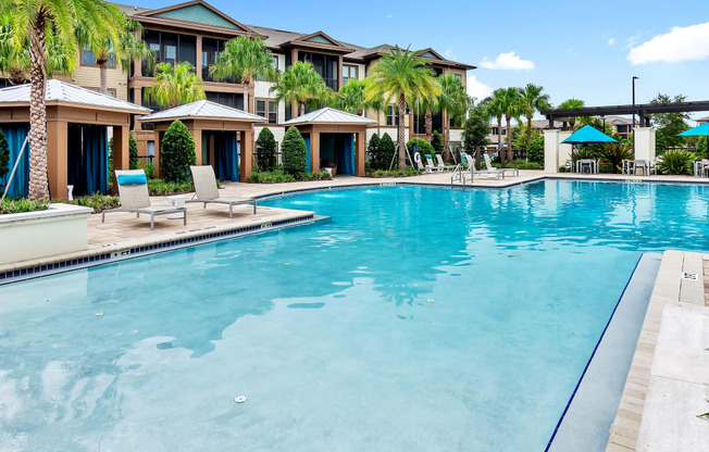 a large swimming pool with lounge chairs and umbrellas in front of a building