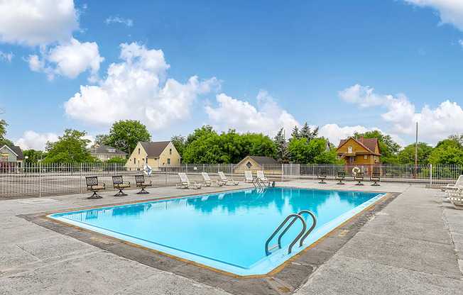 A large outdoor swimming pool surrounded by a fence and lounge chairs.