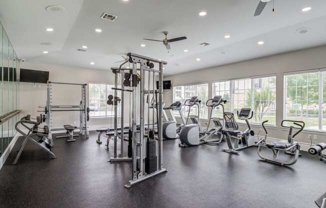 a gym with cardio machines and weights in a building with large windows