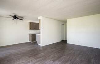 an empty living room with a ceiling fan and a kitchen