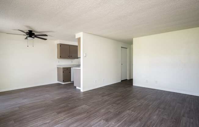 an empty living room with a ceiling fan and a kitchen