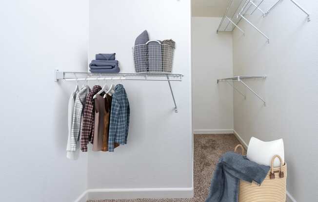 a walk in closet with clothes, a basket with blankets and items on a shelf.