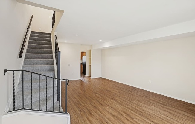 A spacious room with wooden flooring and a staircase with a metal railing.