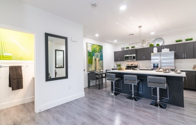 A kitchen with ceiling lights and bathroom and fridge and stools and island and microwave and oven and stove